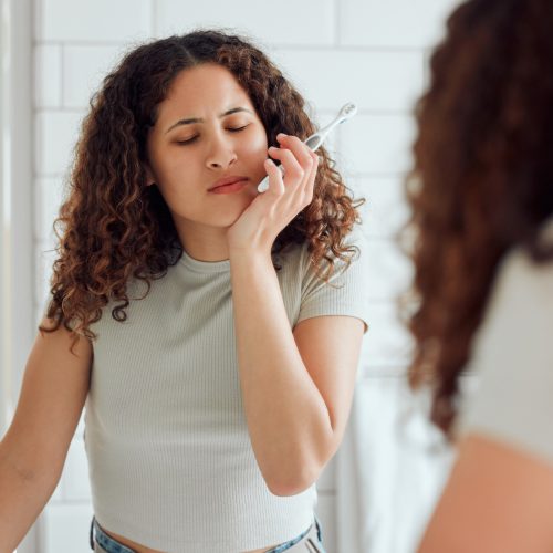 Toothache, oral discomfort and dental sensitivity for a woman in pain while brushing her teeth in the morning. African American female suffering with a painful, hurting or inflammation in her mouth